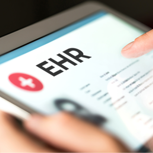 Two hands hold a tablet. The tablet shows the text “EHR” (or electronic health record) at the top.