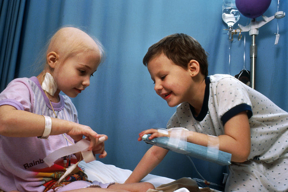 Two child cancer patients sitting on a hospital bed playing with surgical tape.