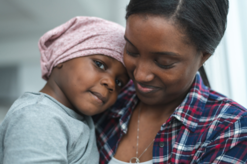 Smiling Black mother holding her young Black child to her chest; child has her head on mother's shoulder and is wearing a pink bandanna around her head.