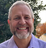 Professional headshot of Granger Sutton smiling at the camera. He's dressed in a purple polo shirt and featured against a wooded backdrop.