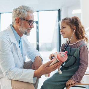 Doctor in white coat with a child patient and stethoscope holding a stuffed animal.
