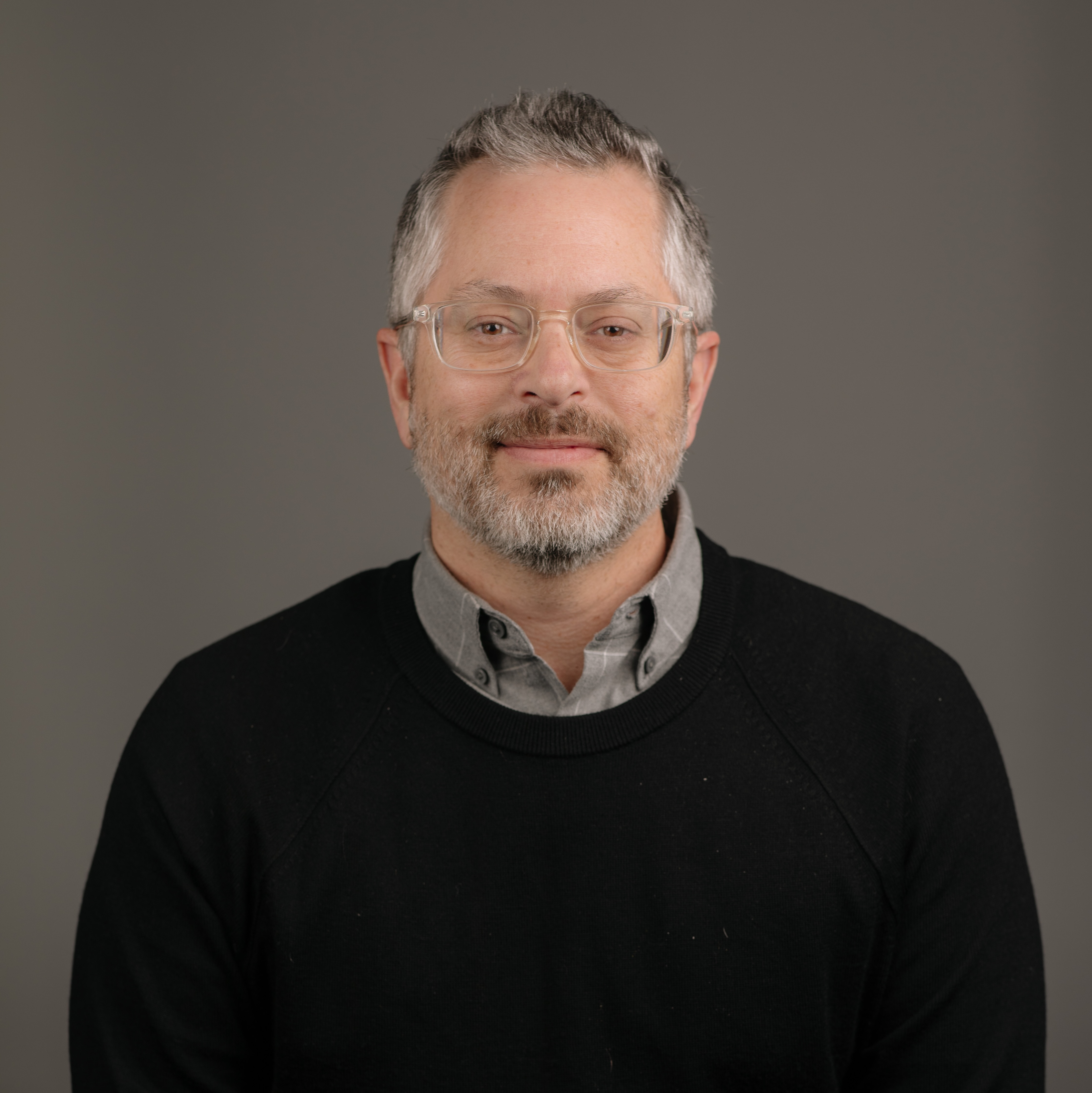 Professional headshot of Dr. Logan Spector, who is smiling at the camera wearing a black sweater against a brown backdrop.